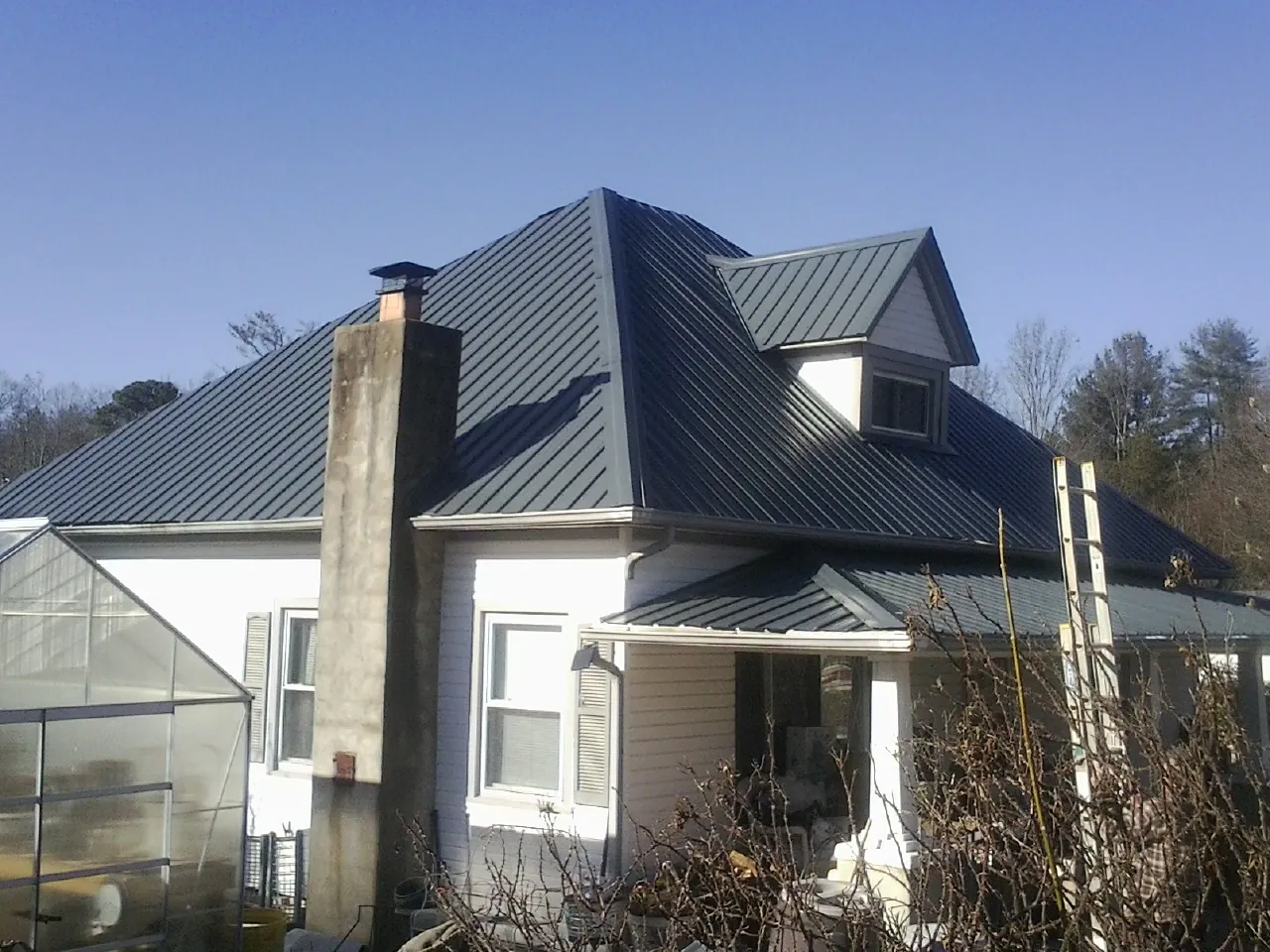 Dark blue standing seam metal roof on a white farmhouse with dormer — Slate & Tile Roof Repair by Roofing Brothers in Hilton