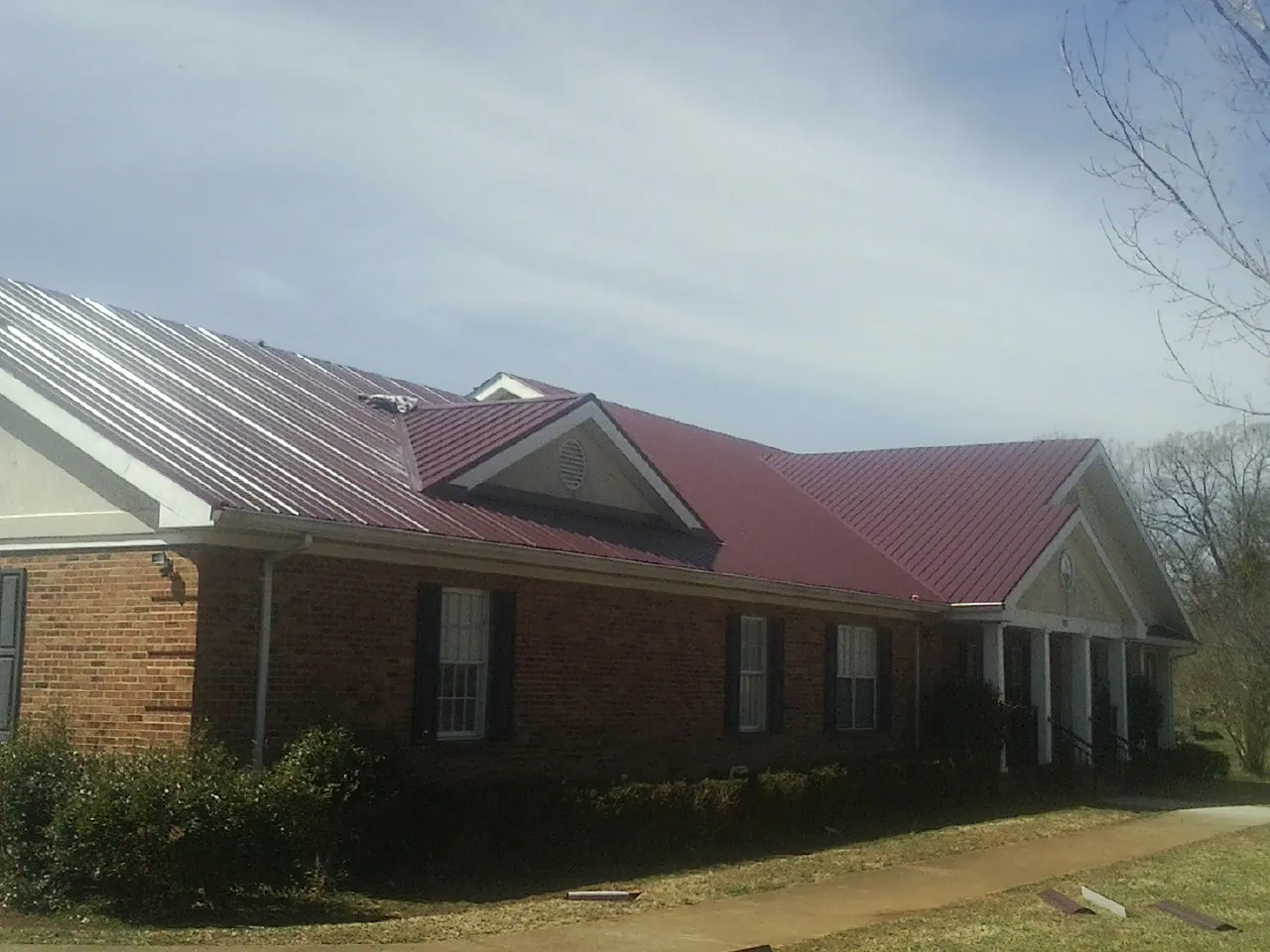 Red metal roof with gabled entries on a long brick building, from a Hail Damage Roof Repair job in Hilton