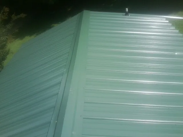 New green metal panels meeting at the ridge of a roof — Flat Roof Repair work by our crew in Hilton