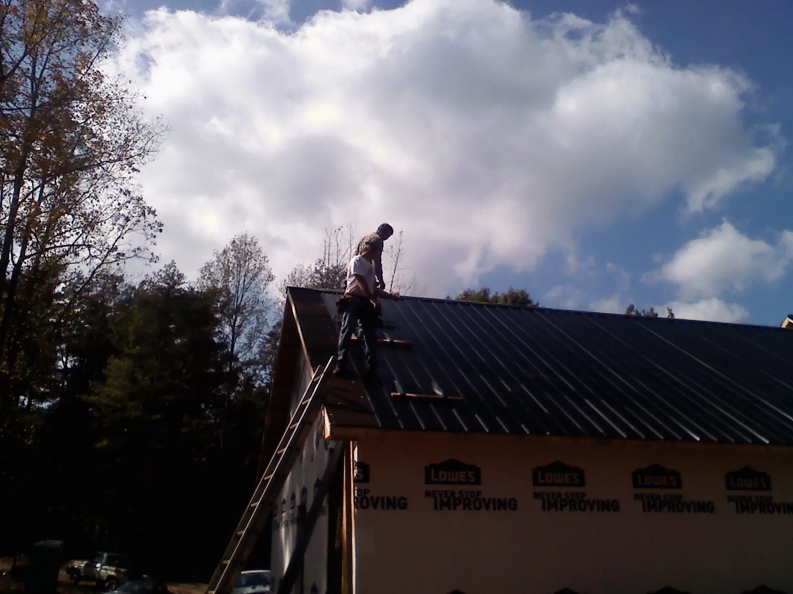 Roofer fastening dark metal panels high against a cloudy sky, from a Roof Inspection job in Hilton