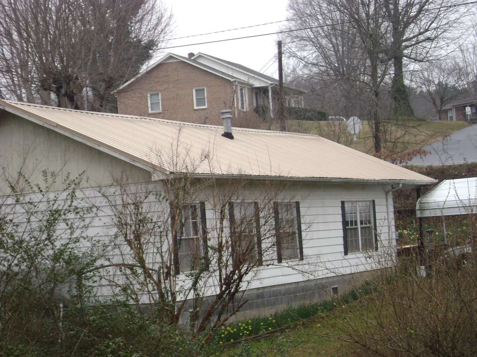 Tan metal roof on a white sided house set into a hillside — Commercial Roofing by Roofing Brothers in Hilton