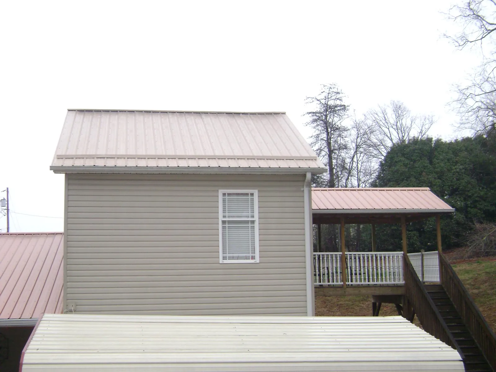 Tan metal roofs on a two story addition and attached porch, from a Roof Replacement job in Hilton